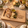 Maple cutting board engraved with gather and an olive sprig, with bread, olive oil and cheese on a candlelit fall table