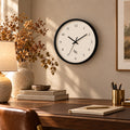 R&R monogram numeral wall clock with a black frame and cream face, above a wooden desk