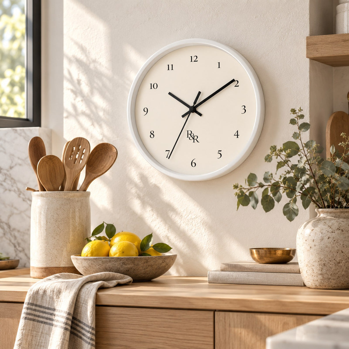 R&R monogram numeral wall clock with a white frame and cream face, in a bright kitchen with lemons