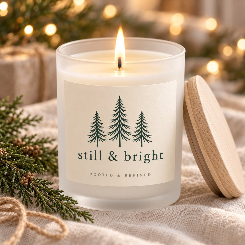 Still & Bright Evergreen Frosted Glass Candle, close-up of the lit candle with its frosted glass, melt pool and maple wood lid on linen