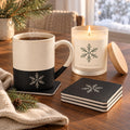 Snowflake coffee lover gift set: engraved speckled mug, matching snowflake coasters and a lit frosted glass candle by a snowy window