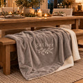 Gather Olive Branch Sherpa Fleece Blanket in Warm Grey by Rooted & Refined, draped over a dining bench