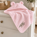 Pink bear-ear baby hooded towel with an embroidered olive branch, on a white nursery dresser
