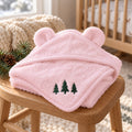 Pink bear-ear baby hooded towel with three embroidered green evergreen trees, on a wooden stool in a nursery
