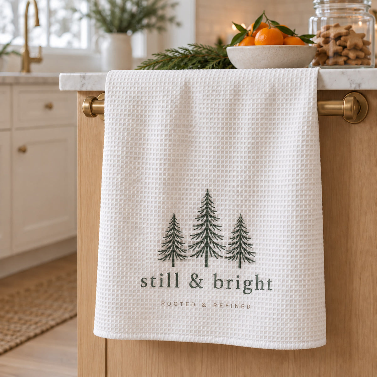 Still & Bright Evergreen Waffle Tea Towel in white by Rooted & Refined, hanging from a brass towel bar in a holiday kitchen