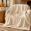 Pumpkin Sherpa Fleece Blanket in ivory by Rooted & Refined, draped over an armchair in a fall living room