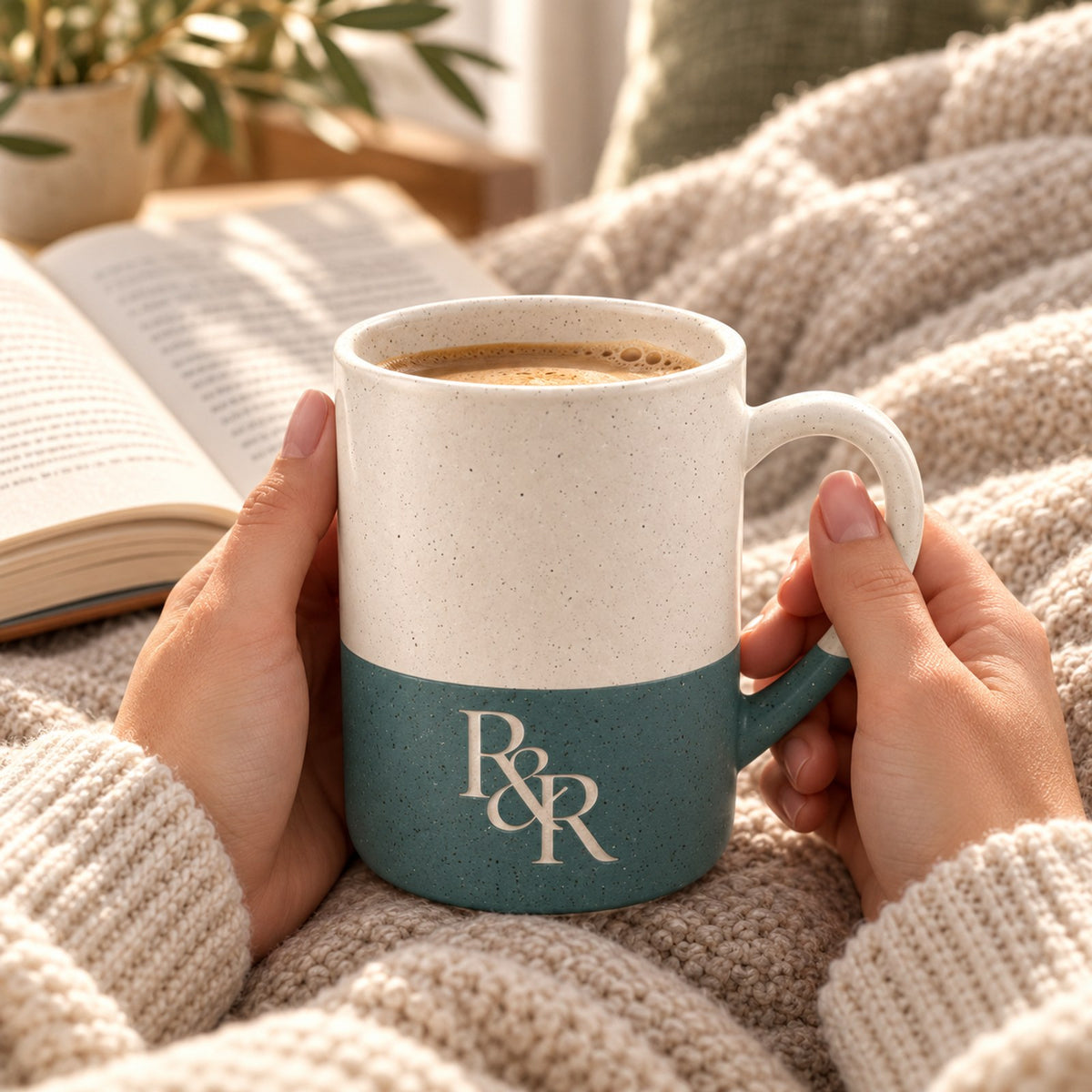 R&R monogram engraved speckled mug in Forest Green held in hands over a knit blanket
