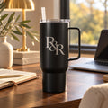 Black 40 oz tumbler with handle engraved with an R&R monogram, on a modern desk