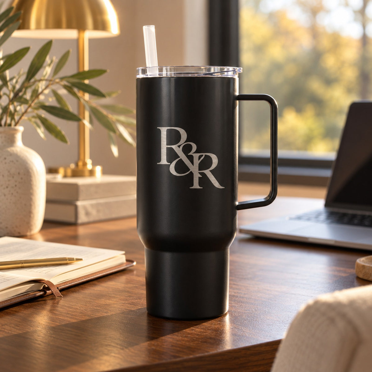Black 40 oz tumbler with handle engraved with an R&R monogram, on a modern desk