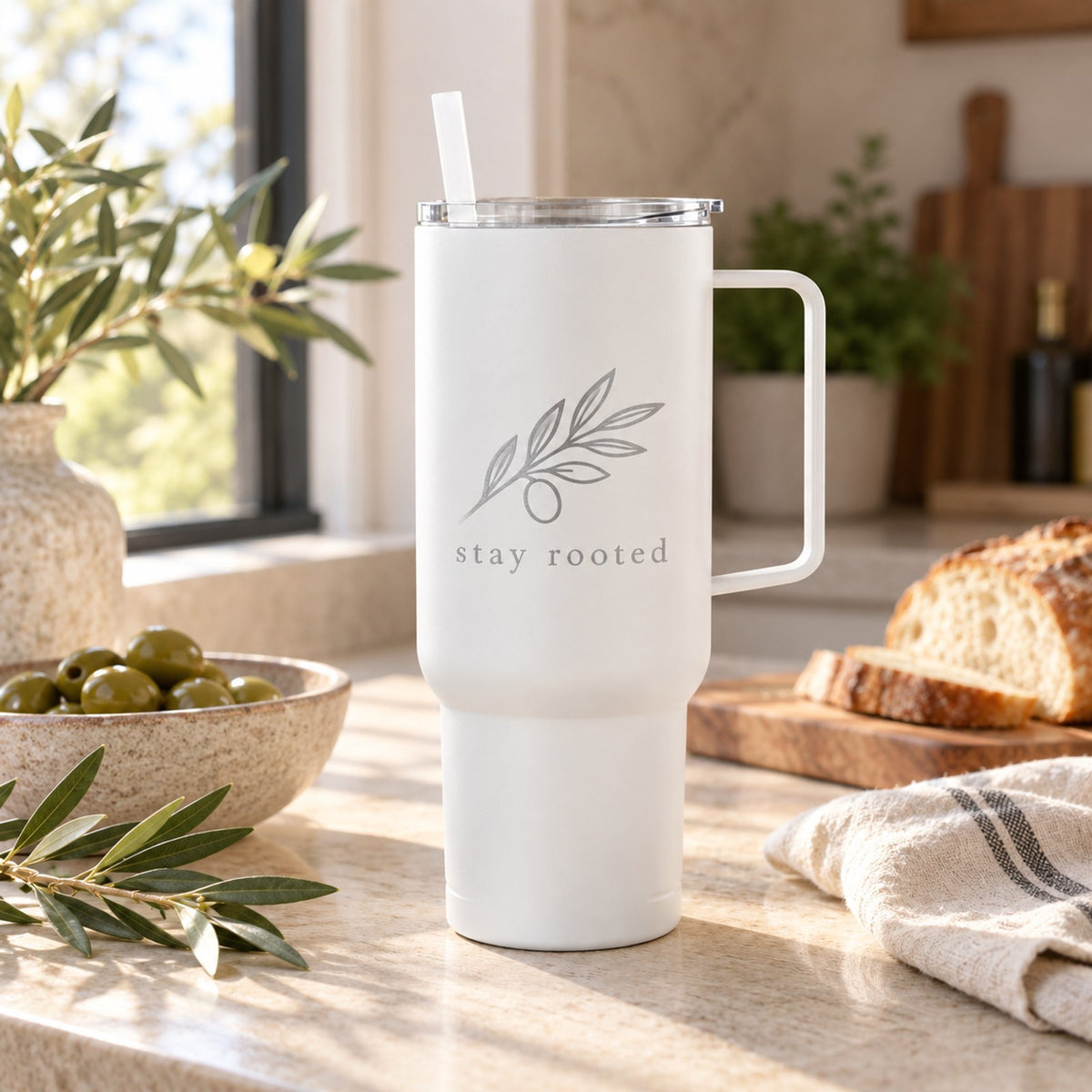 White 40 oz tumbler with handle engraved with an olive branch, on a kitchen counter