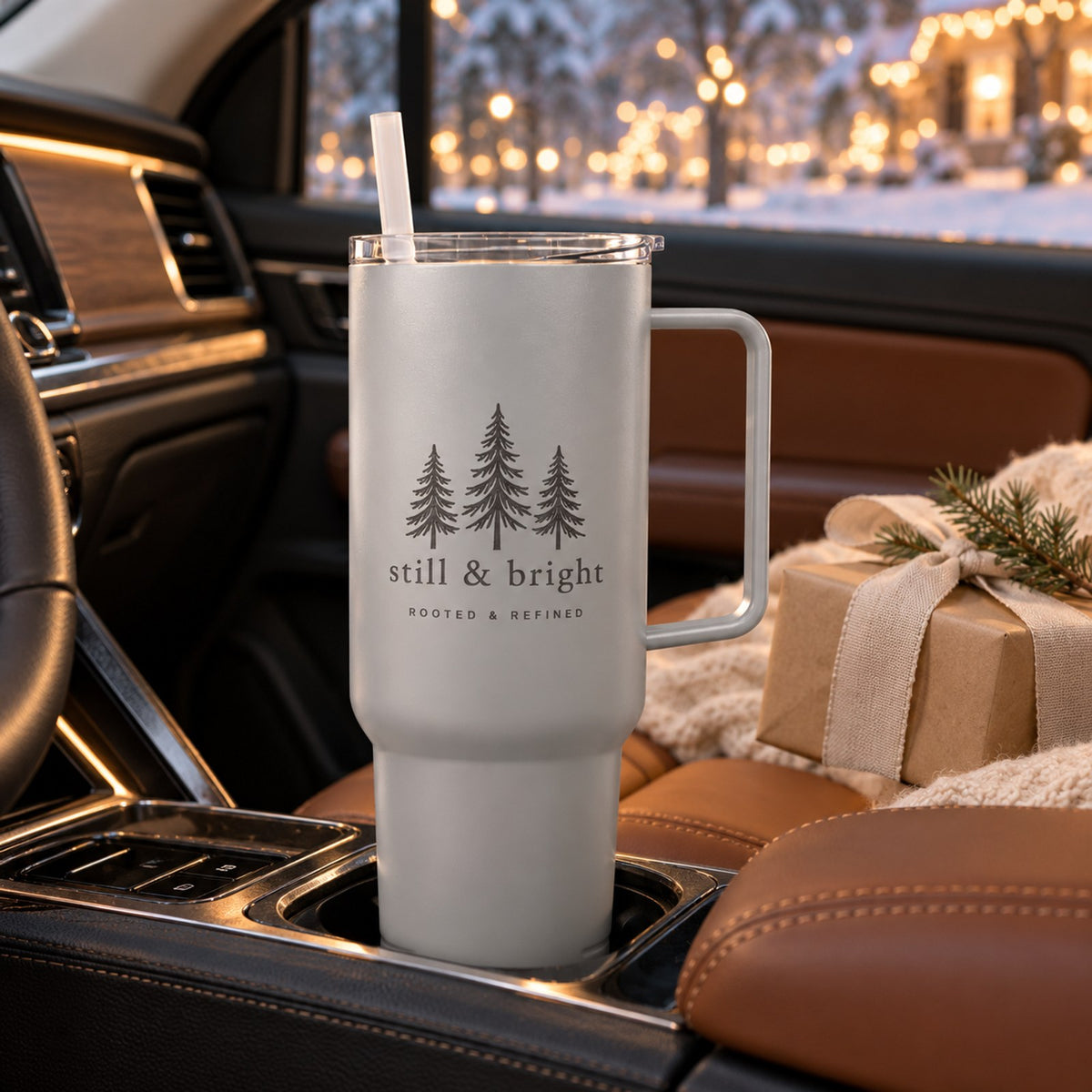 Gray 40 oz tumbler with handle engraved with three evergreen trees and still & bright, in a car cup holder